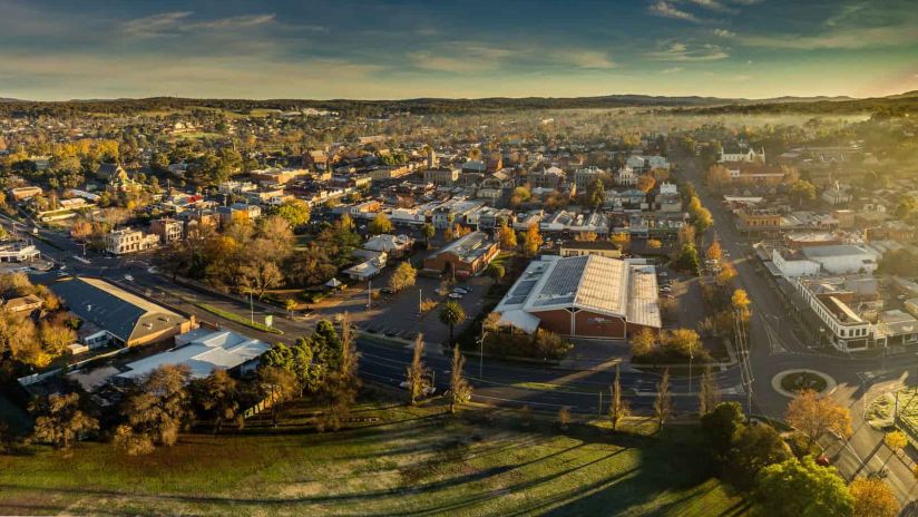 An aerial photograph of a regional Australian town at dawn, with sunrise appearing to the east as fog lifts across the town.